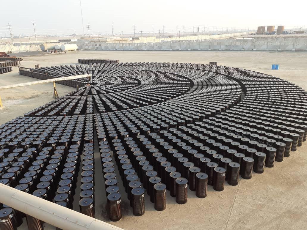 Thousands of new steel bitumen drums standing in concentric arcs across an open filling yard, photographed from height